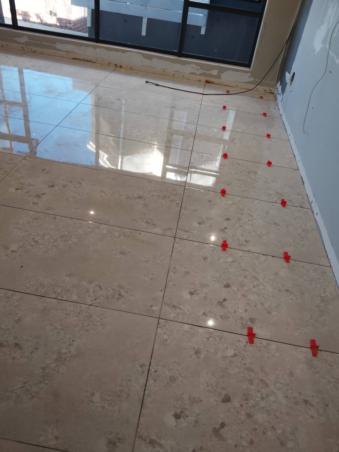 Large floor tiles being installed with red leveling clips